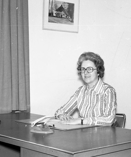 Vera de Kort zit als medewerkster van de gemeente achter haar bureau met papieren, perforator en telefoon, Vught (foto: collectie Vera Delleman-de Kort, collectie BHIC nr. 1923-004100)