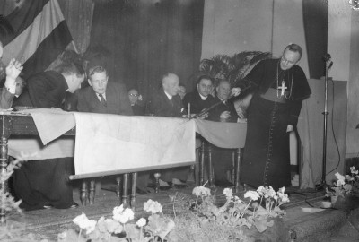 Geestelijke wijst een plek in Canada aan op de landkaart bij de sluiting van een emigratiecursus, Veghel 1951