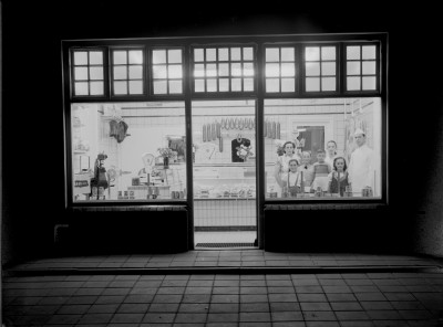 De winkelruiten van Slagerij de Laat, met vlak achter het glas het slagersgezin zelf. Dinther 1955
