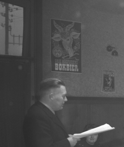 Docent De Bok, met buiten het raam al electriciteitskabels en boven zijn hoofd... reclame voor Bok-bier!