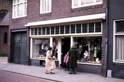 Veel bruin, oranje, groen en blauw in de etalage van 'De Gouden Spin' van Riet van Leusden naast de Petruskerk. Vught ca. 1978
