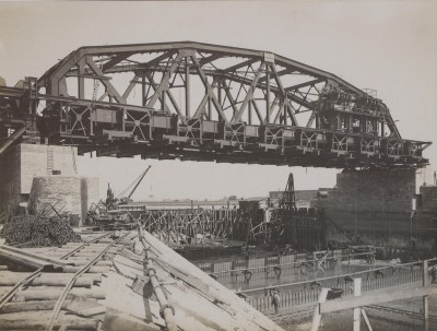 De sluis en brug bij Grave in aanbouw. Onder het brugdeel is de rivierbedding droog gemaakt met damwandprofielen. In de zo ontstane bouwput op de rivierbodem wordt de betonnen drempel gebouwd waar de stuwschuiven en hun schuifconstructie komen te rusten. Grave 1927 (foto: fotograaf onbekend, collectie BHIC, nr. GRA1166)