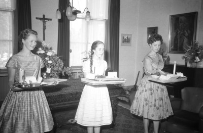 Meisjes bieden verschillende rookwaren aan op het zilveren jubileum van pastoor Cox. Op het blad staat ook een kaars op meteen op te kunnen steken. Den Dungen, 1959