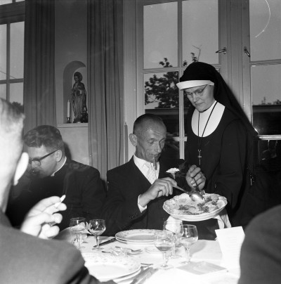 Wethouder Marinus Bax met een sigaar in de mond, tijdens het eten bij het 60-jarig priesterfeest van pastoor Kluytmans. Liempde, 1959