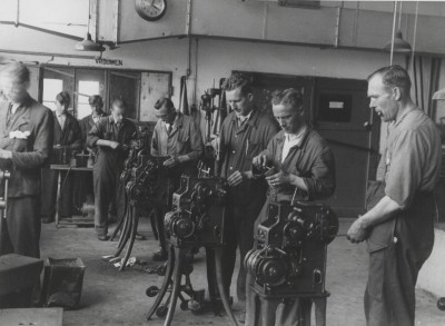 Arbeiders bedienen apparatuur in een fabriek, terwijl sigaretten/pijp roken. Schijndel, ?