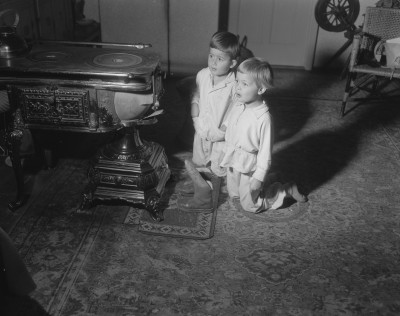 Twee kinderen zingen bij de kachel voor Sinterklaas. Plaats onbekend, 1956