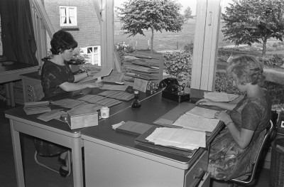 Dames aan het werk op kantoor met stapels papier, stempels en een telefoon met draaischijf, Geffen 1964 (foto: Fotopersbureau Het Zuiden, collectie BHIC nr. 1636-000362)