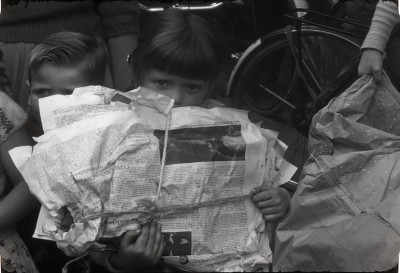 Een meisje houdt een pak papier met oude kranten vast. Haaren, 1958