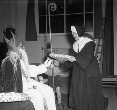 Sint geeft een cadeau aan een zuster bij kindertehuis Huize Sint Agnes. Uden, 1956