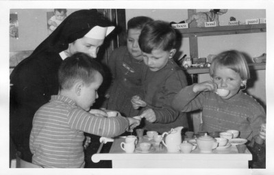 Zuster Jacinta met kinderen met oor-telefoontjes in haar voorschoolklas, Sint-Michielsgestel ca. 1950 ( (foto: Erfgoedcentrum Nederlands Kloosterleven, archief Dochters van Maria en Joseph (AR-Z032), inv.nrs 833 en 890)