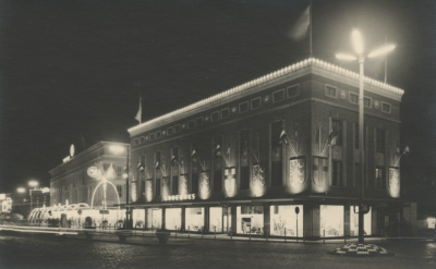 De bevrijdingsherdenking een avondopname van de feestverlichting van het 18 Septemberplein. Met modewarenhuis C&A en woonwinkel Lodewijks, 09-1954