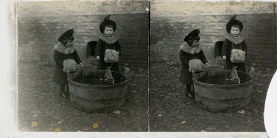De kinderen Frans en Felix Dor gekleed in jas met bontkraag en mof staan bij een houten tobbe waarin een zeilbootje drijft., omstreeks 1904